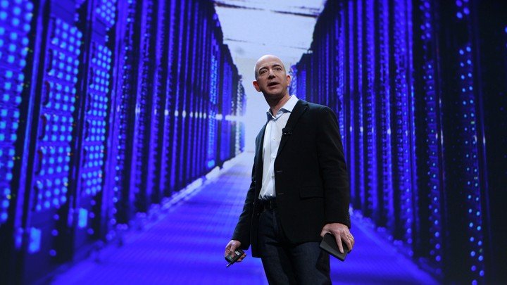 Jeff Bezos stands in front of a purple, blue, and black data center.