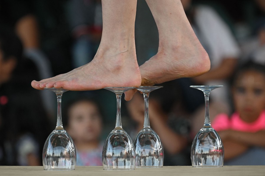 A performer in bare feet balances atop four wine glasses.
