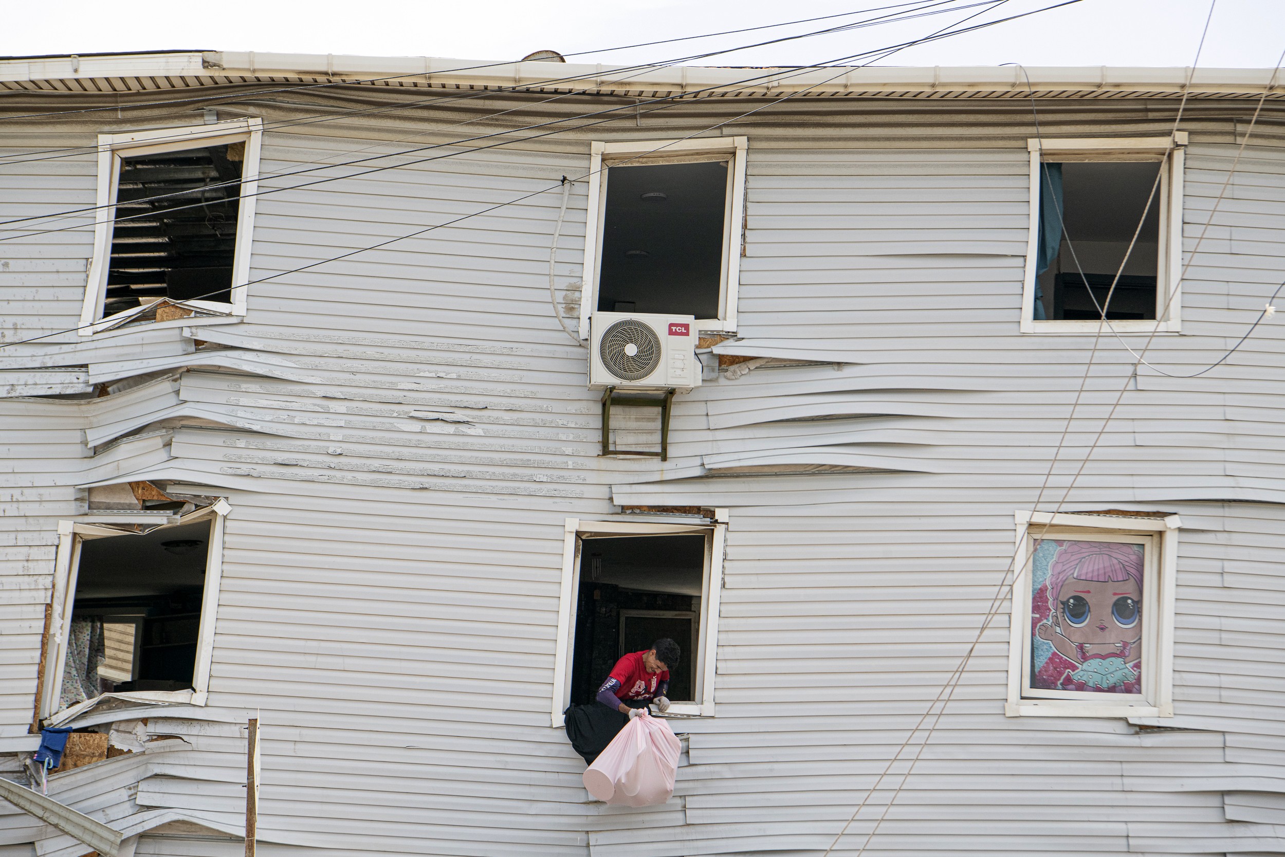 A man recovers belongings from a heavily-damaged house, lowering items from an open window.