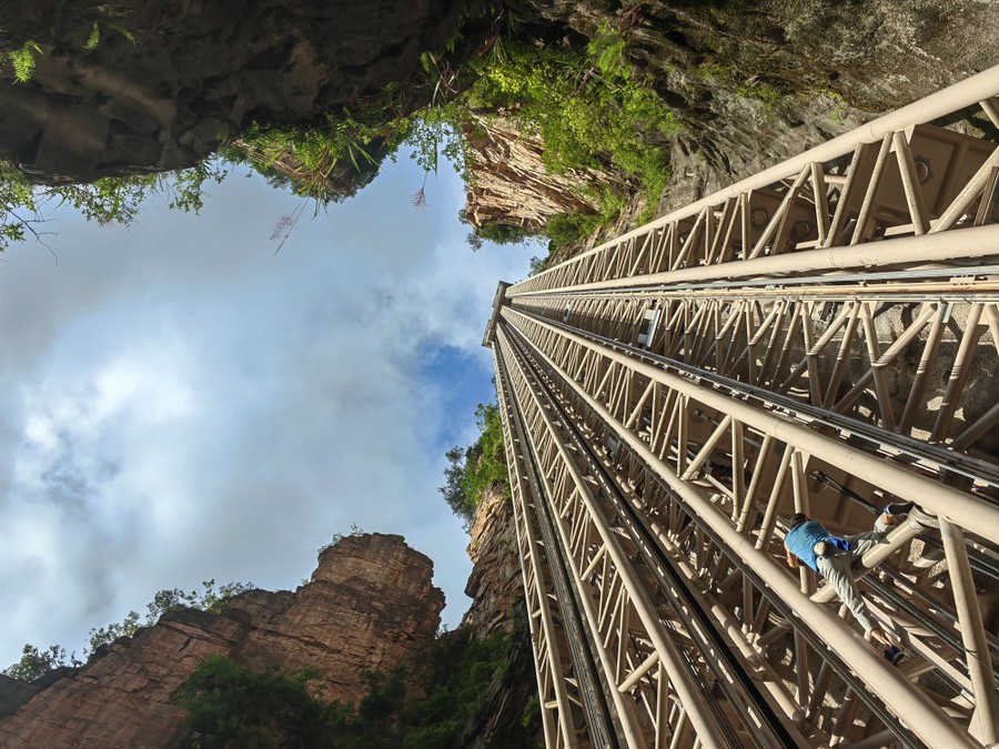 A person climbs on the lower part of a very tall steel structure that rises along a sheer cliff.
