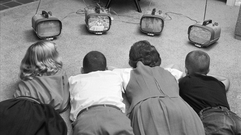 Old black-and-white photograph of four kids lying on a carpet, watching four small televisions