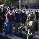 A group of people stand together in a street, confronting masked federal officers during an immigration raid.
