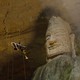 A person rappels into a cavern in front of a huge stone carving of a head.