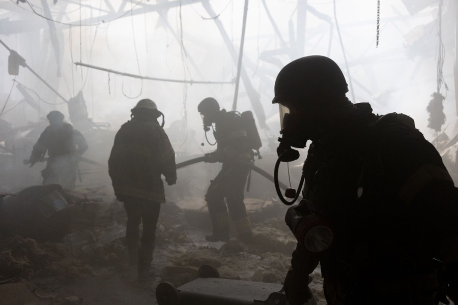 Several firefighters wearing protective masks work inside a damaged and smoke-filled building.