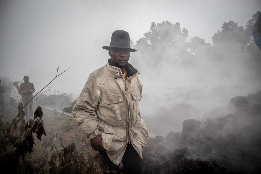 Men walk past still-smoking volcanic rocks.