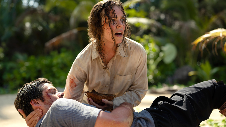 Rachel McAdams holds a bloody Dylan O'Brien in one hand and half of a coconut in another on a tropical island.