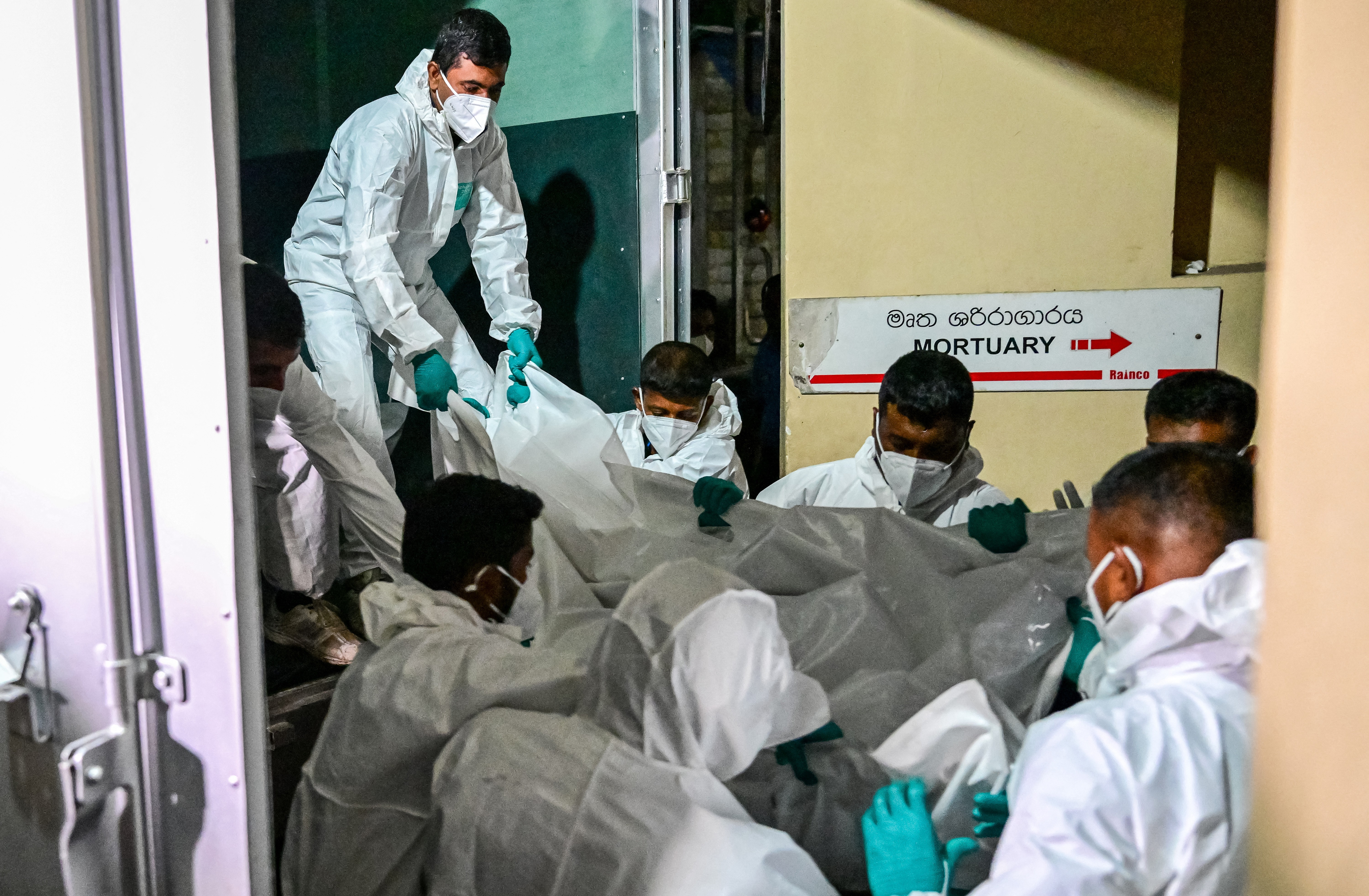 Workers wearing protective suits carry bagged bodies from a truck into a mortuary.