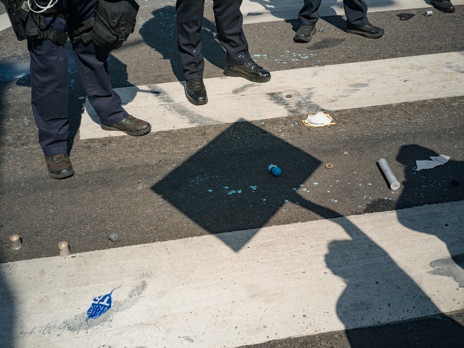 Police stand in a line while the shadow of a person holding a sign is next to them on the ground.