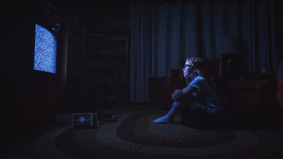 A child with red hair and glasses sits on the floor in front of a staticky TV screen