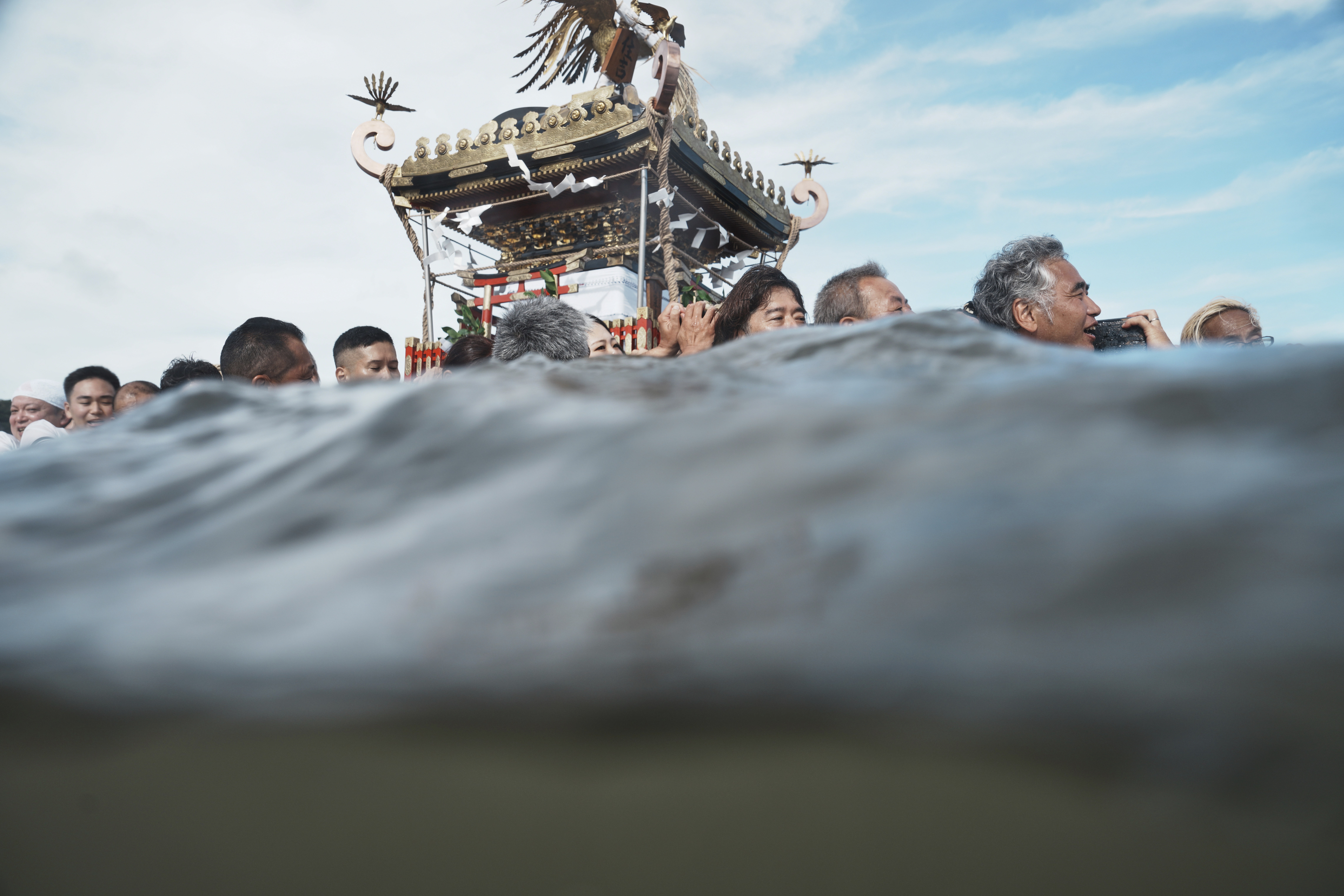 Worshippers carry a portable shrine into the sea, seen from the water's surface.