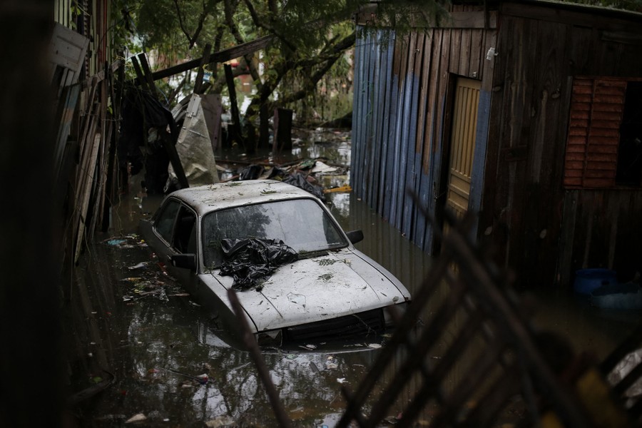 A car sits partially submerged in floodwater alongside damaged houses.