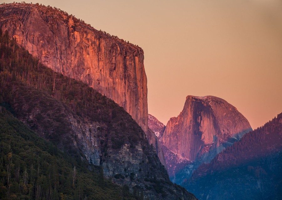 Sunset and haze color the steep mountain faces in Yosemite National Park a pinkish color.
