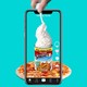 A phone records a hand spraying whipped cream into a can of Spaghetti-Os on top of a pizza.