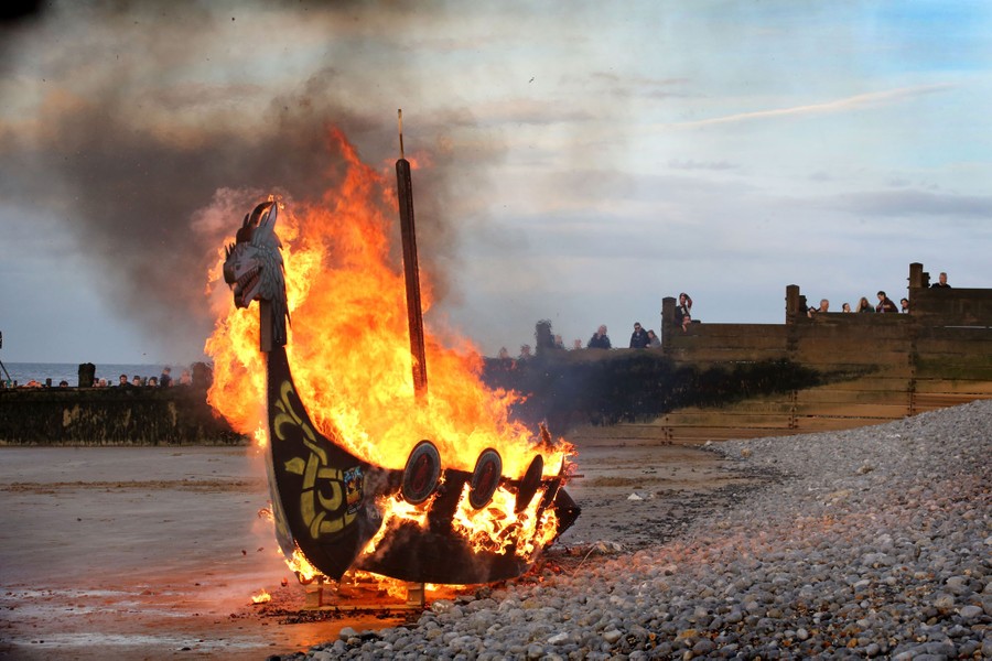 A replica Viking longship burns on a shoreline.