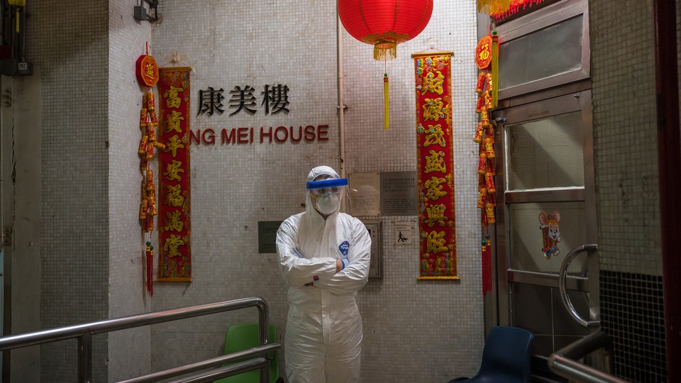 An official wearing protective gear stands guard outside an entrance to the Hong Mei House residential building at Cheung Hong Estate in the Tsing Yi district, on February 11, 2020 in Hong Kong, China