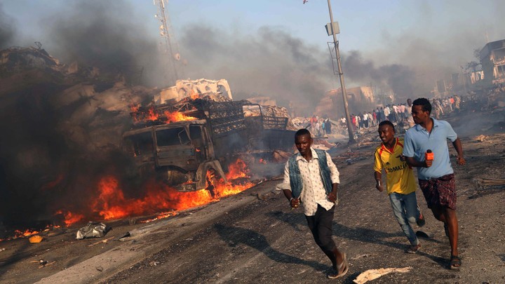 Three civilians run away from the scene of an explosion.