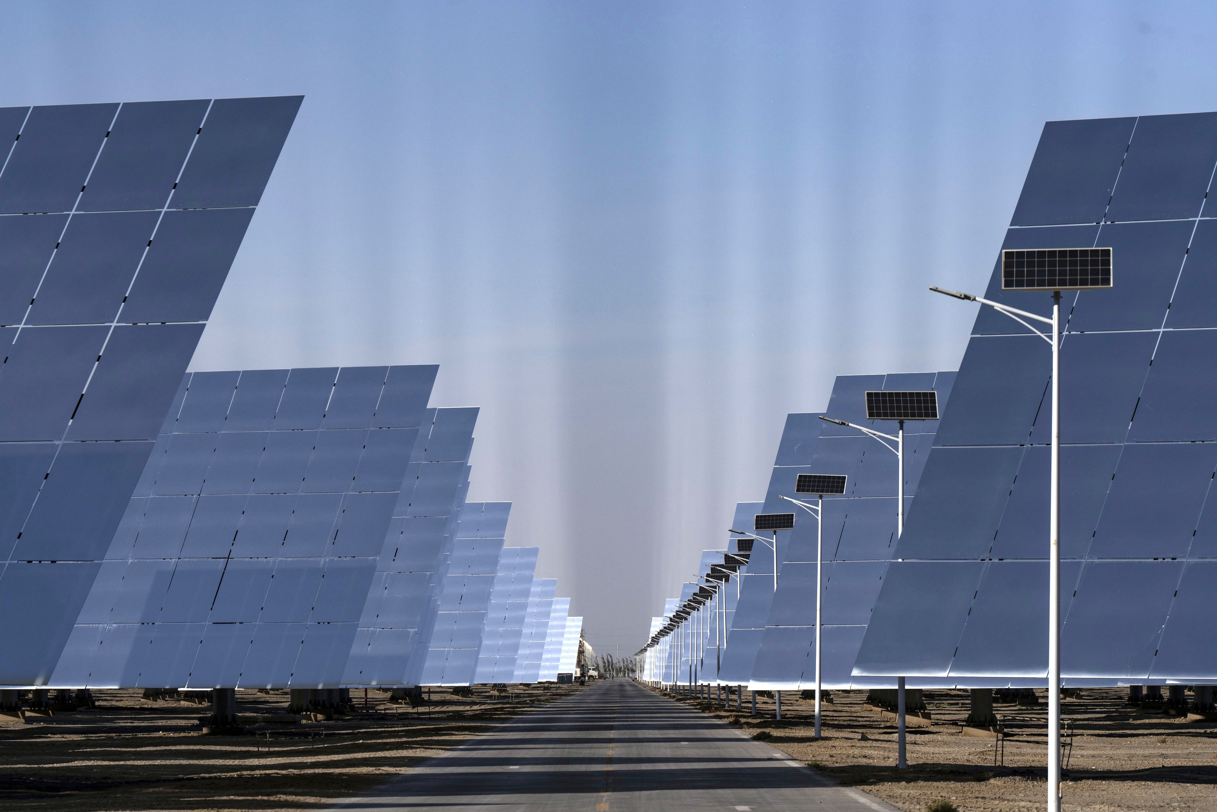 Many solar panels reflect sunlight, visible as rays in the sky above them.
