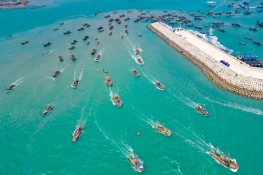 Dozens of fishing boats depart a harbor at the same time.