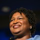 Stacey Abrams looking into the distance. She is smiling and wearing a blue dress.