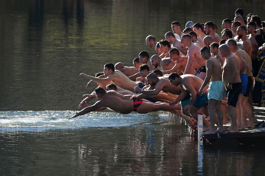A group of men in bathing suits leap from a dock into a lake.