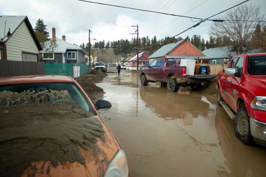 Cars and a street are covered in mud after a flood, in a residential neighborhood.