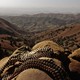 Bandoliers rest on sandbags in the foreground, overlooking a rocky valley.
