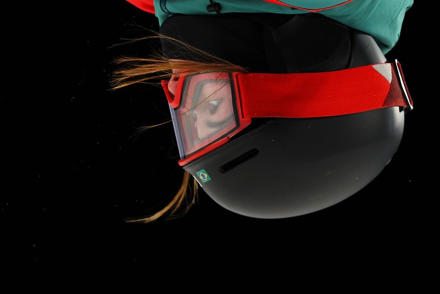 A close view of a helmeted skier, seen upside-down during a jump.