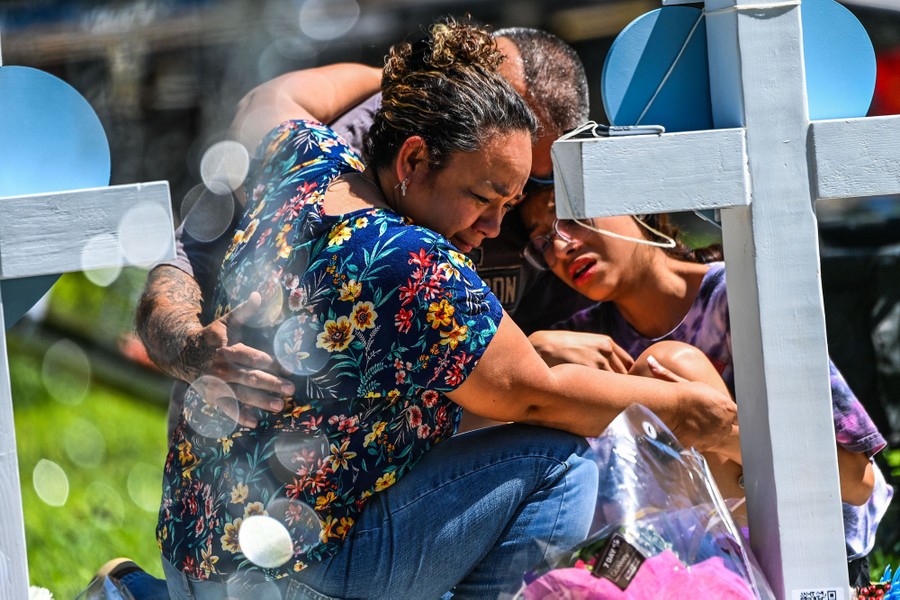 Several people hold one another as they kneel at a makeshift memorial.