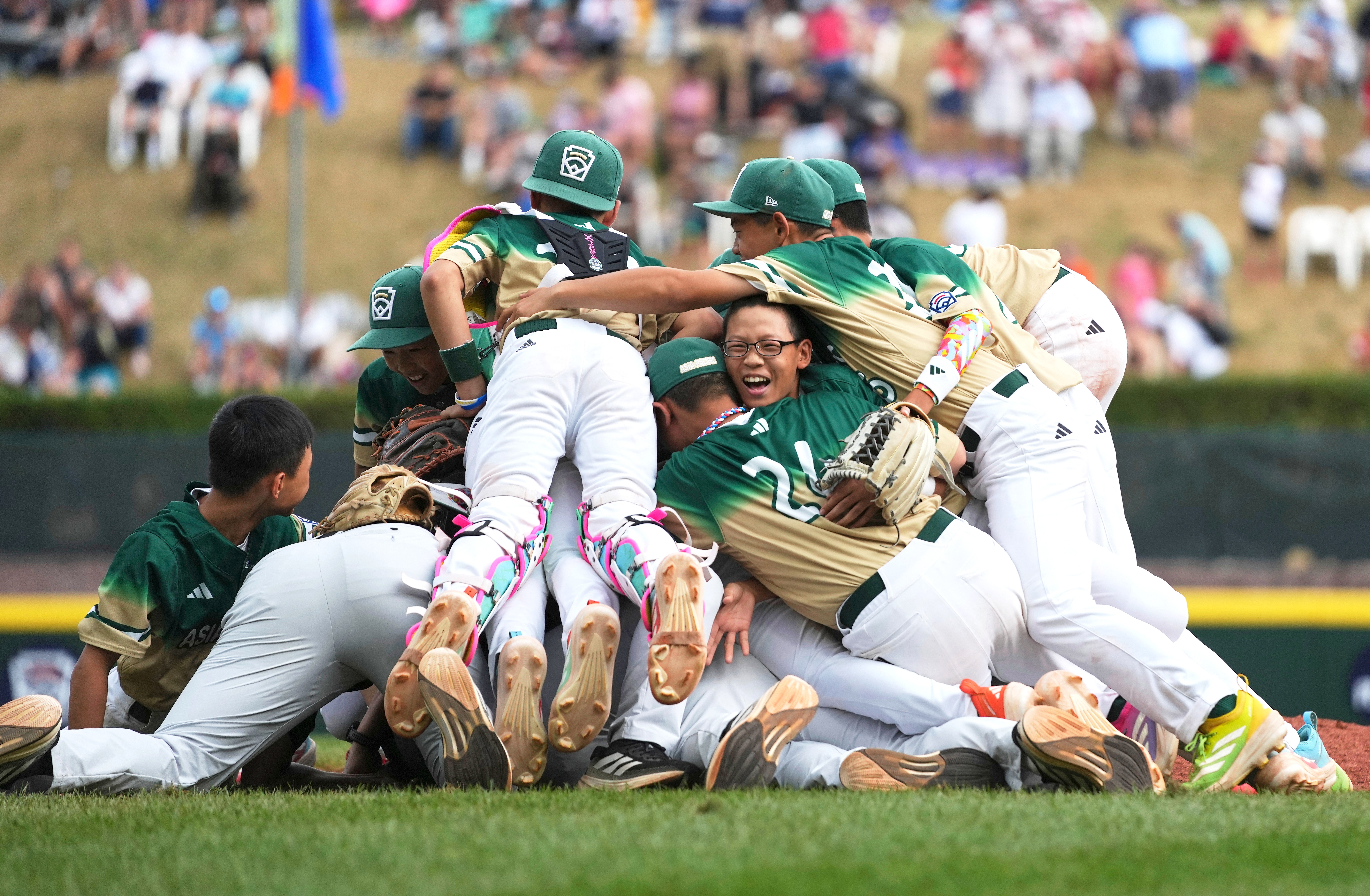 Young baseball players jump on top of each other, piled up in celebration.