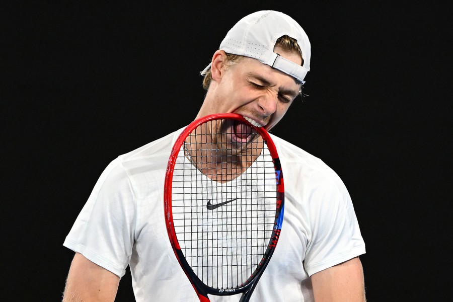 A tennis player bites his racket.