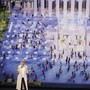An Apple speaker stands in front of a screen depicting people gathered in a town square