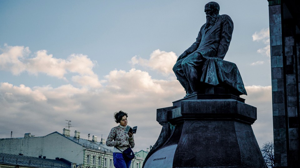 A girl reading a book walks by a statue of Dostoyevsky.