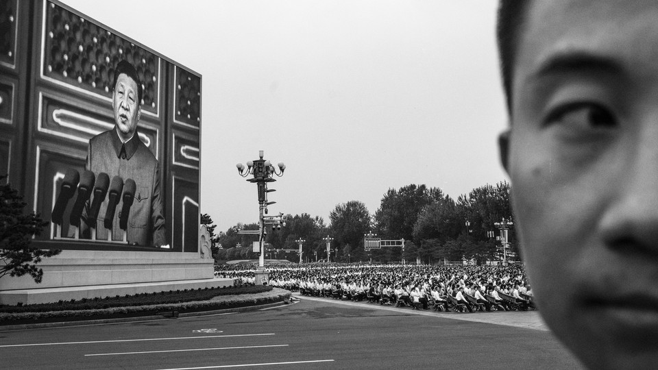 A black-and-white photo of Xi Jinping appearing on a huge screen at a rally in China.