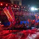 A crowd looks on while people ride and row in a long, thin boat decorated with a dragon's head on its bow.