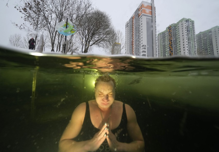 A woman is seen swimming underwater in a nearly frozen lake.