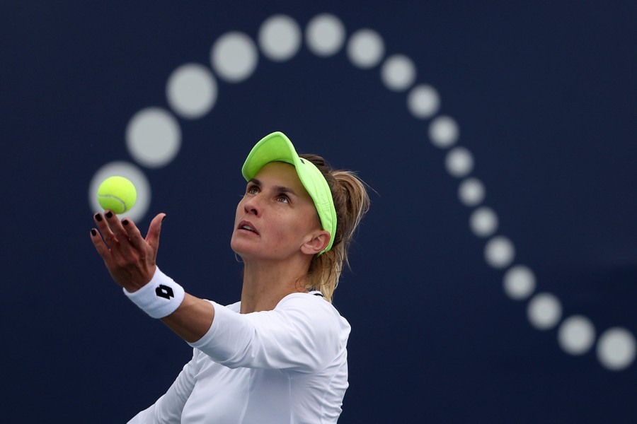 A tennis player prepares a serve, the ball blending with a swooping display in the background.