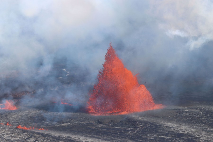 A large fountain of lava rises above the floor of a volcanic crater.