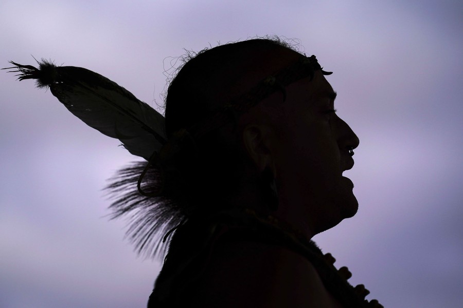 A person is seen in silhouette, wearing traditional Native American adornments.