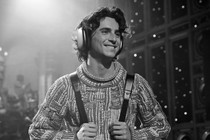 Timothée Chalamet wearing a thick knit sweater holding backpack straps and wearing over-ear headphones, in black and white