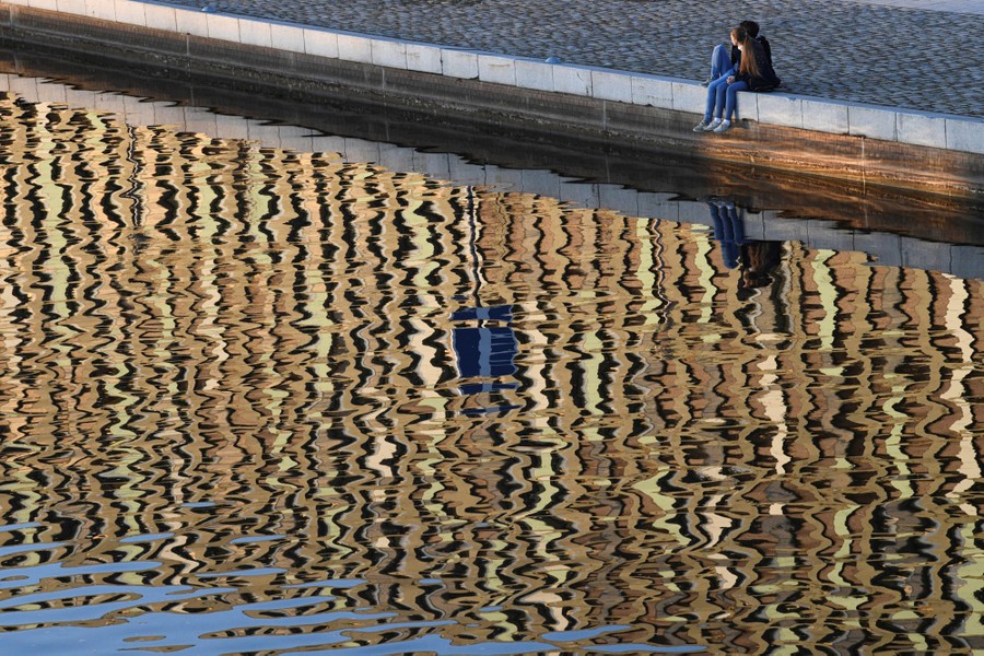 People sit on a paved riverbank.