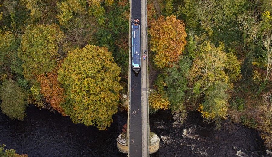 An aerial view of a canal boat crossing an aqueduct bridge over a river