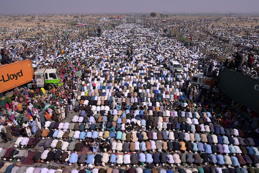 Hundreds of people kneel side-by-side in prayer, covering most of a large road.
