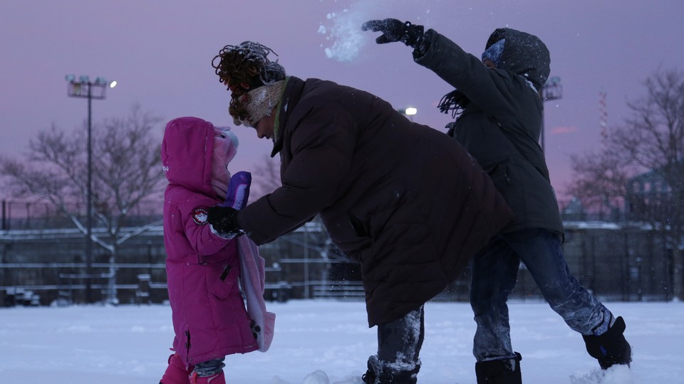 An adult comforts one child while another throws a snowball behind them. 