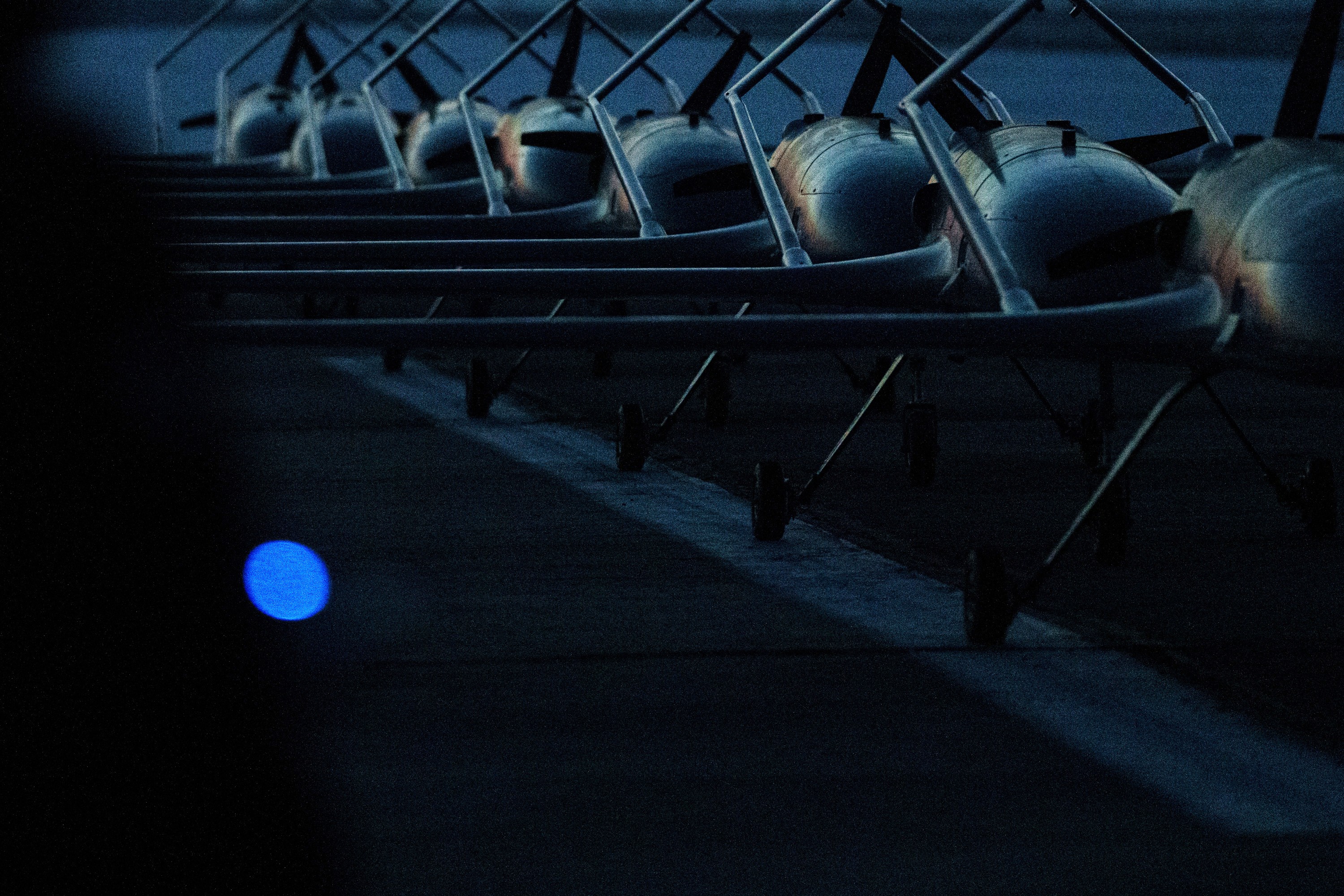 Eight airplane-shaped attack drones sit, lined up, on a runway.