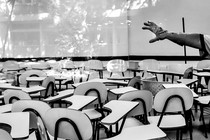 A hand wearing a cleaning glove gestures in a classroom filled with empty tablet-arm chairs.