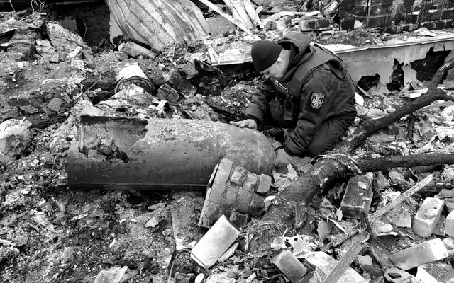 A man crouches next to unexploded ordnance in Ukraine.