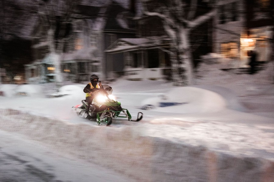 A person rides a snowmobile along a snow-covered residential street.