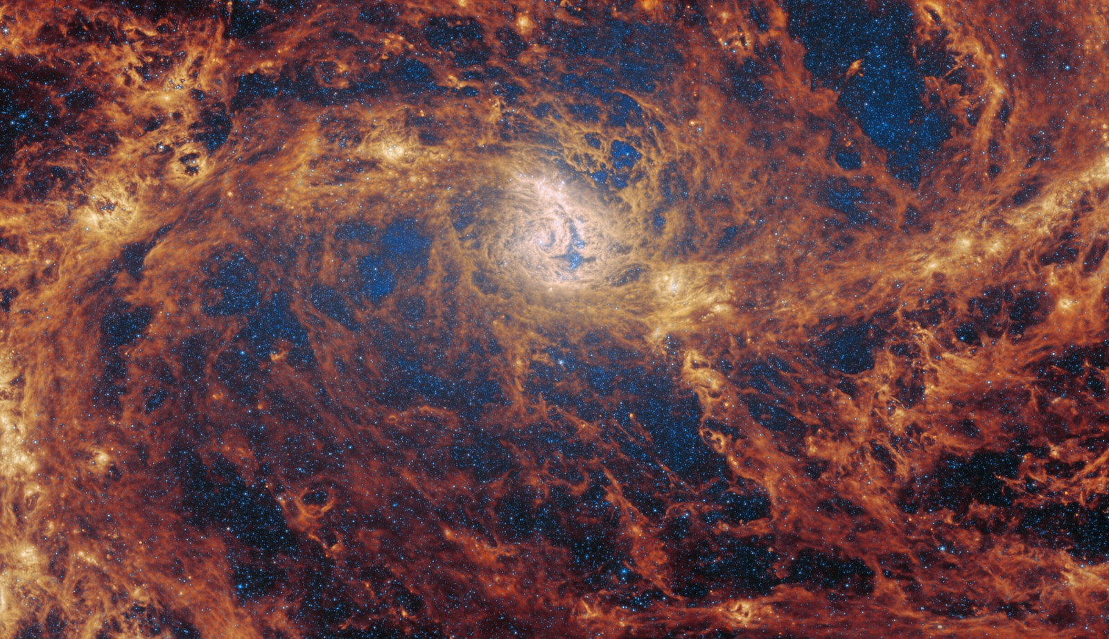 A tight view of the swirling center of a distant spiral galaxy, dominated by billowing yellowish-orange streams of gas and dust