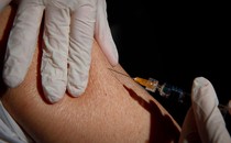 a gloved hand injecting a needle into an arm
