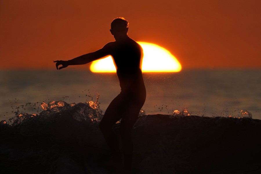 A surfer rides a wave as the sun sets over the ocean.